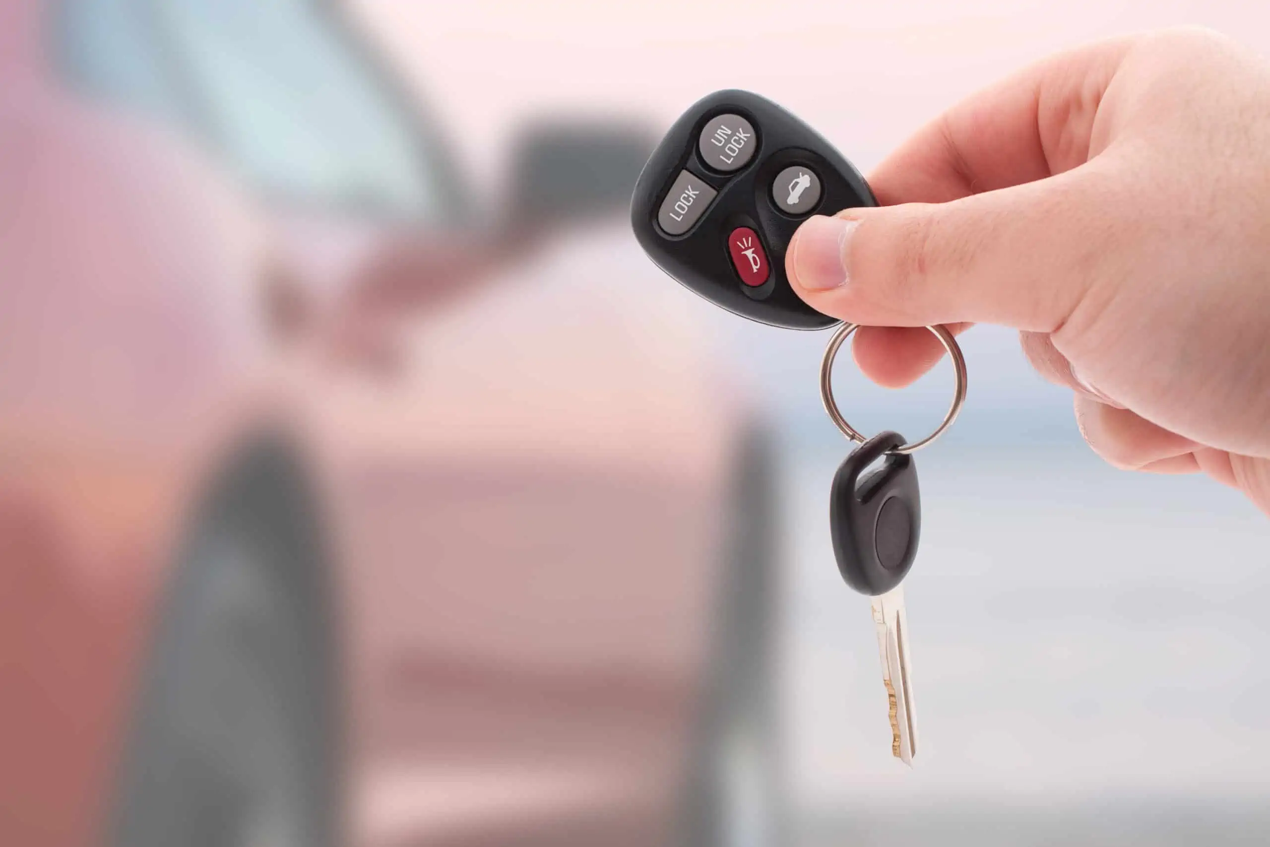 Hand holding keyring with car key and car keyfob in front of a blurred car.