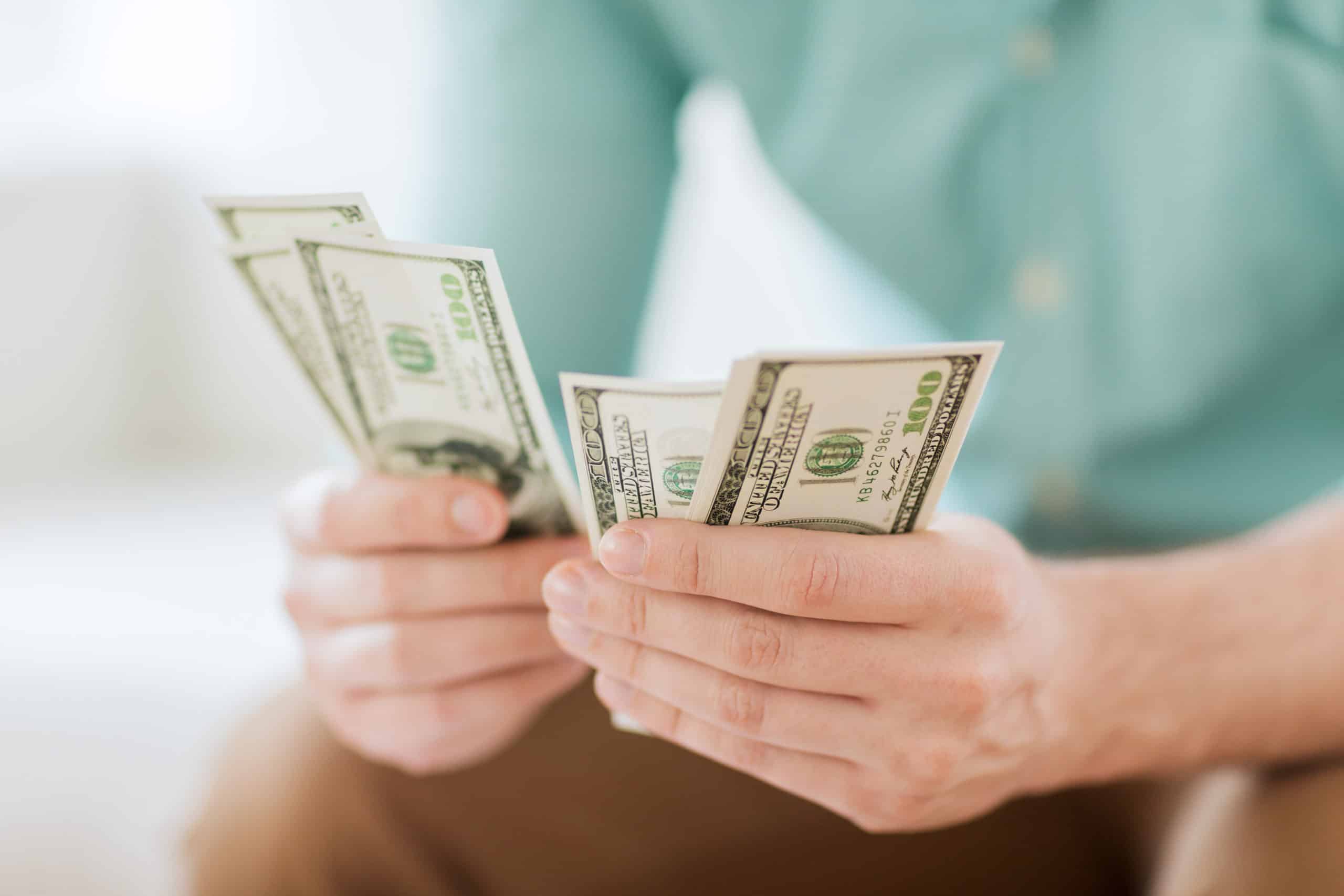 Man's hands holding $100 bills budgeting money