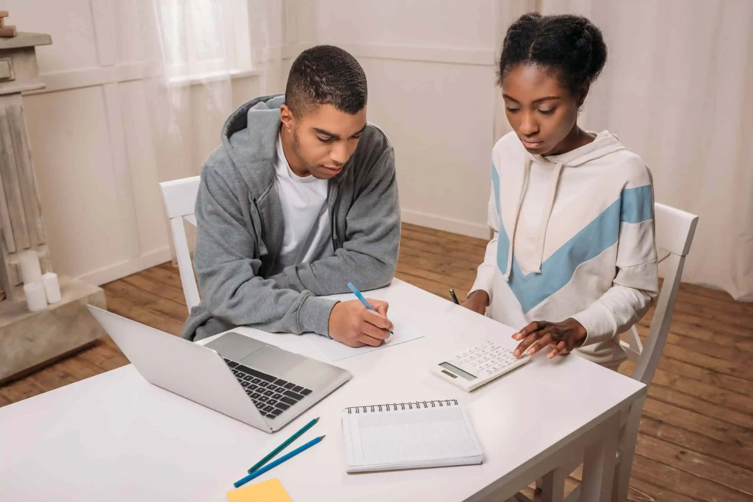 Black couple sitting at a white nesting table calculating how much of a credit card balance transfer they can do