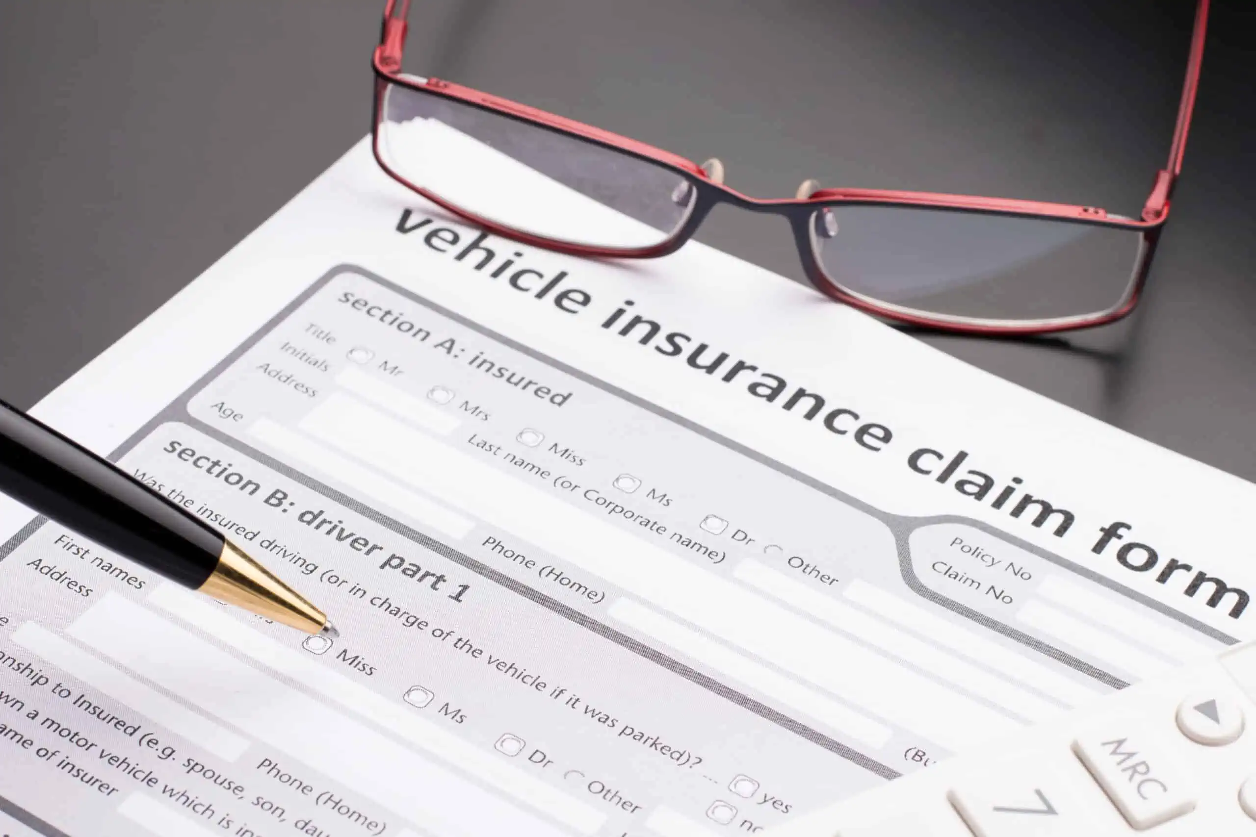 Car insurance claim form with a black lacquer ballpoint pen and red reading glasses.