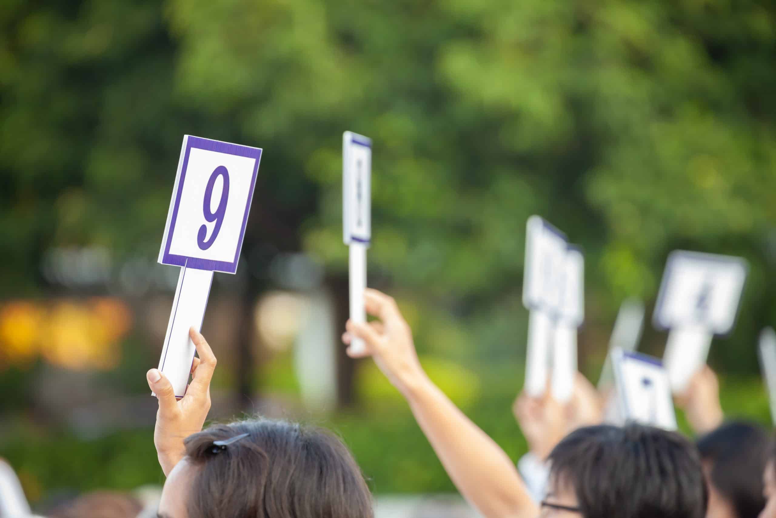 Bidders at charity auction holding up placards unaware that it may not be considered a charitable contribution for taxes.