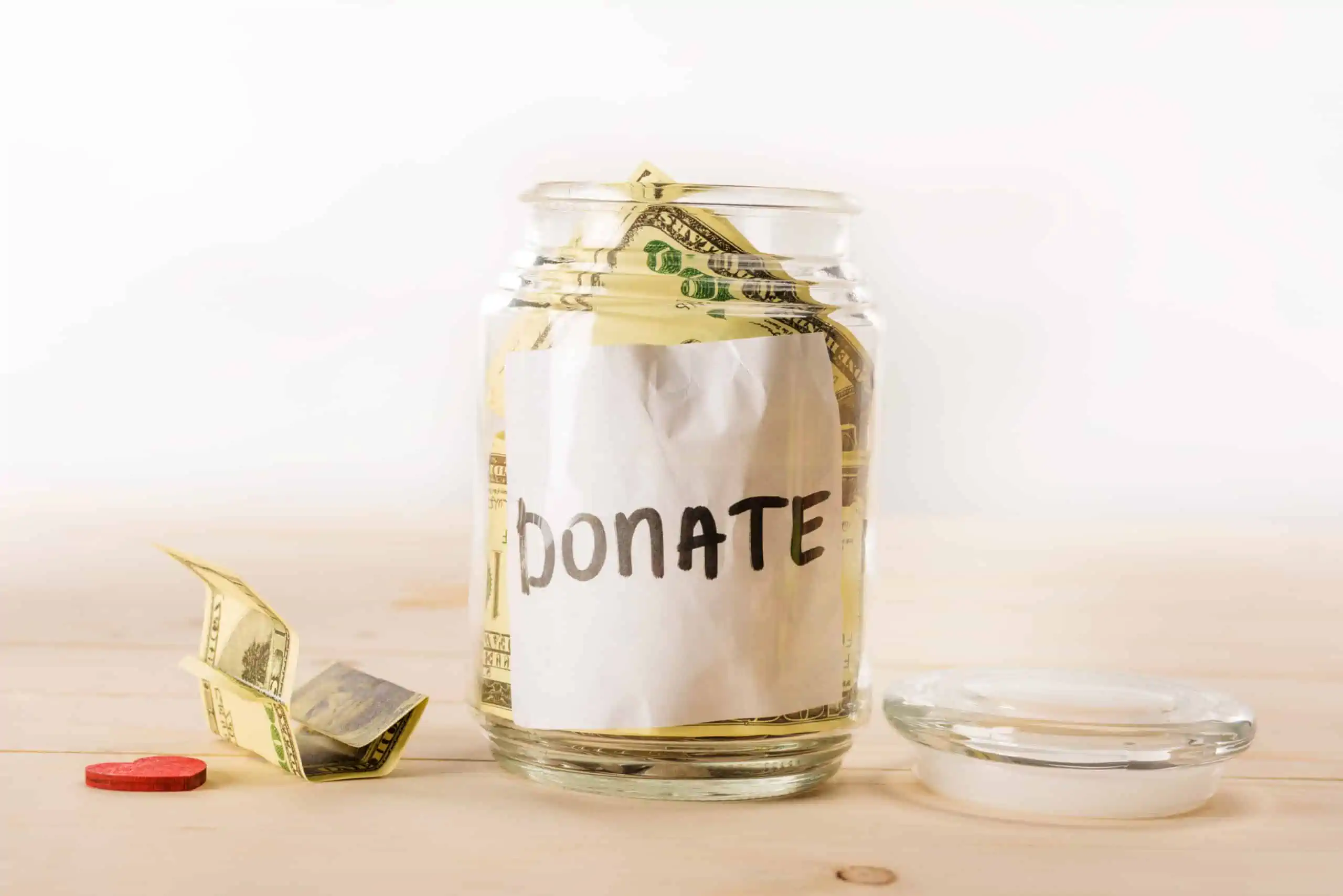 Glass jar with white "Donate" label stuffed with $100 bills to make charitable contributions