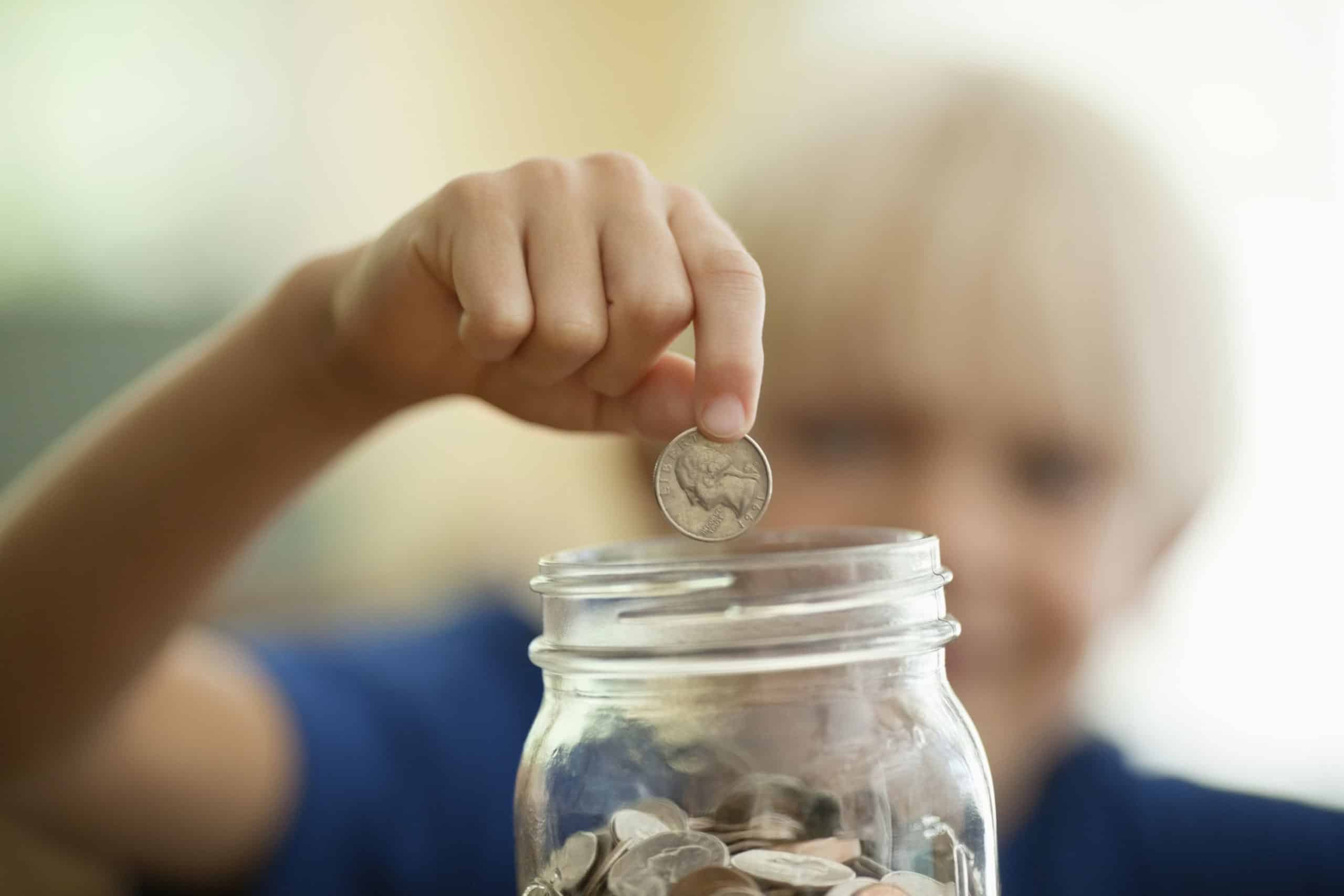 Young blonde boy wearing a dark blue t-shirt saving change in a glass Ball jar