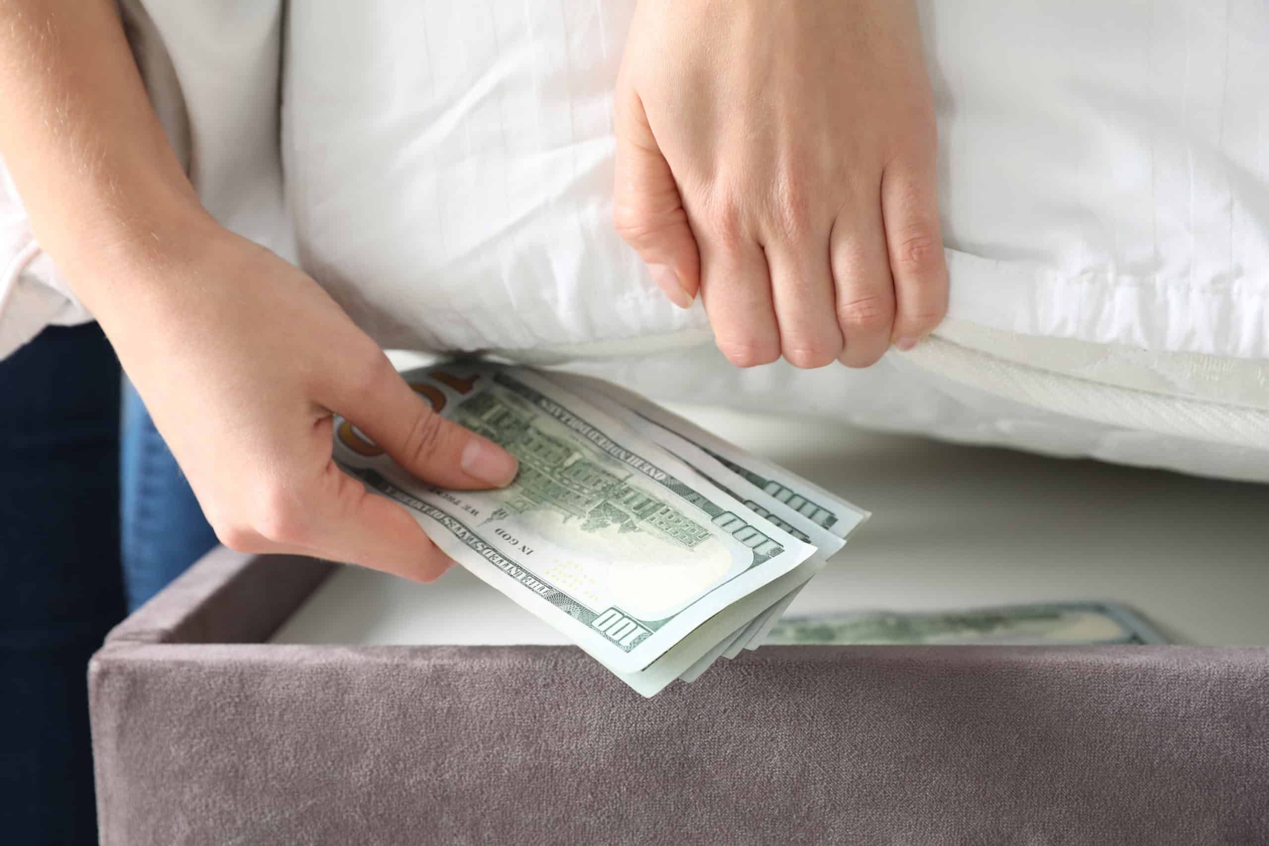 Caucasian woman putting hundred dollar bills under a mattress to have during emergencies.