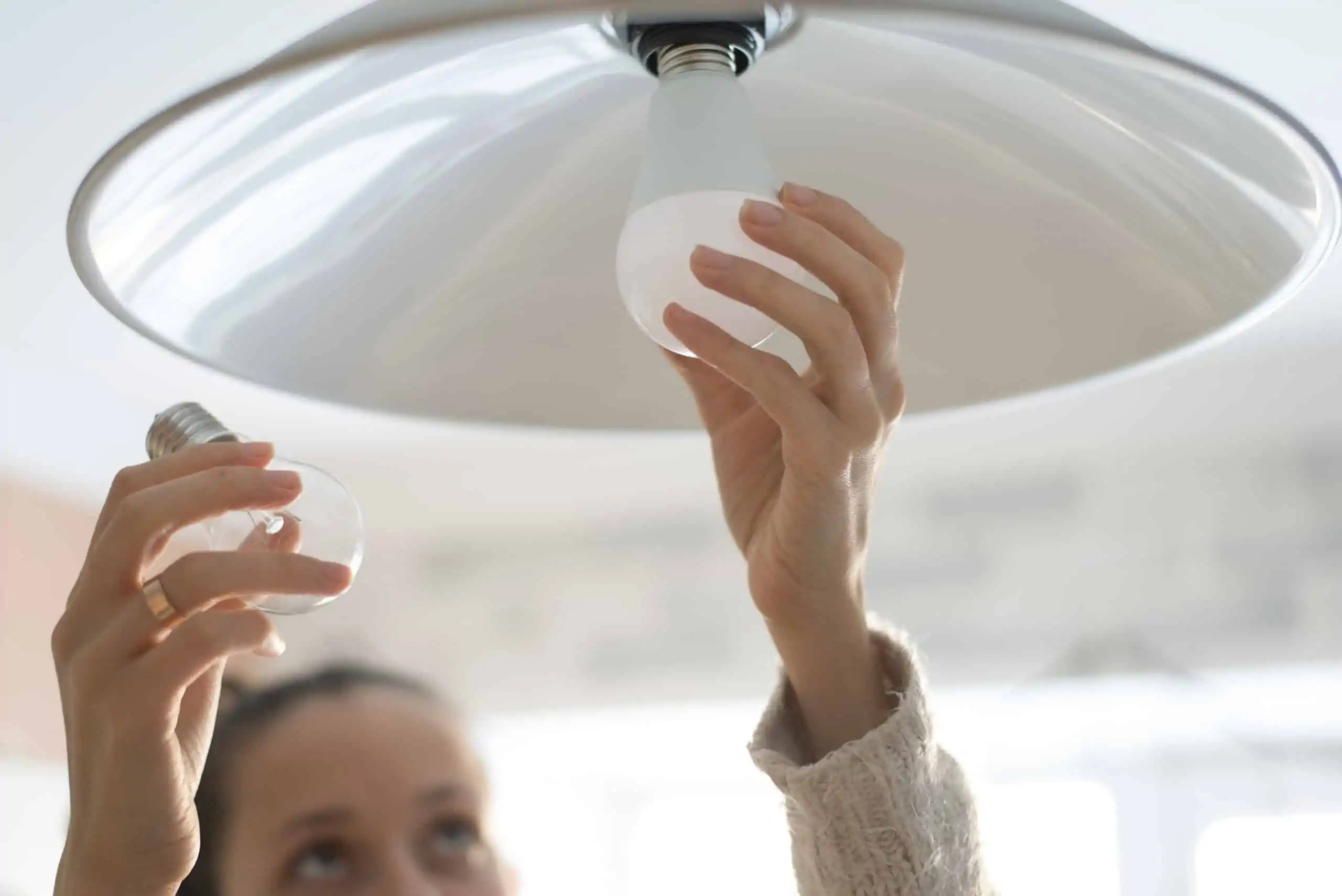 Woman replacing old incandescent light bulbs with LED light bulbs using less lighting energy and lowering utility bills