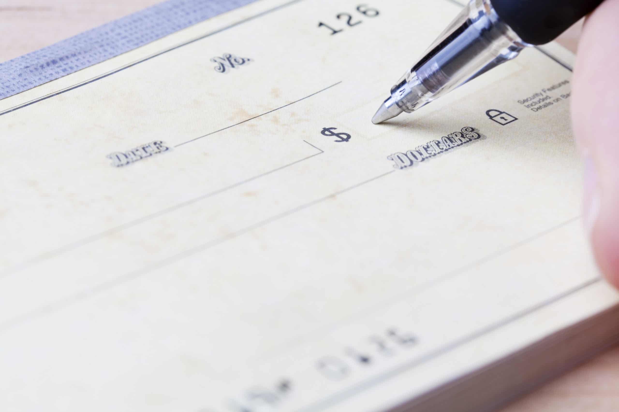 Closeup of a hand filling out a check with a black ballpoint pen