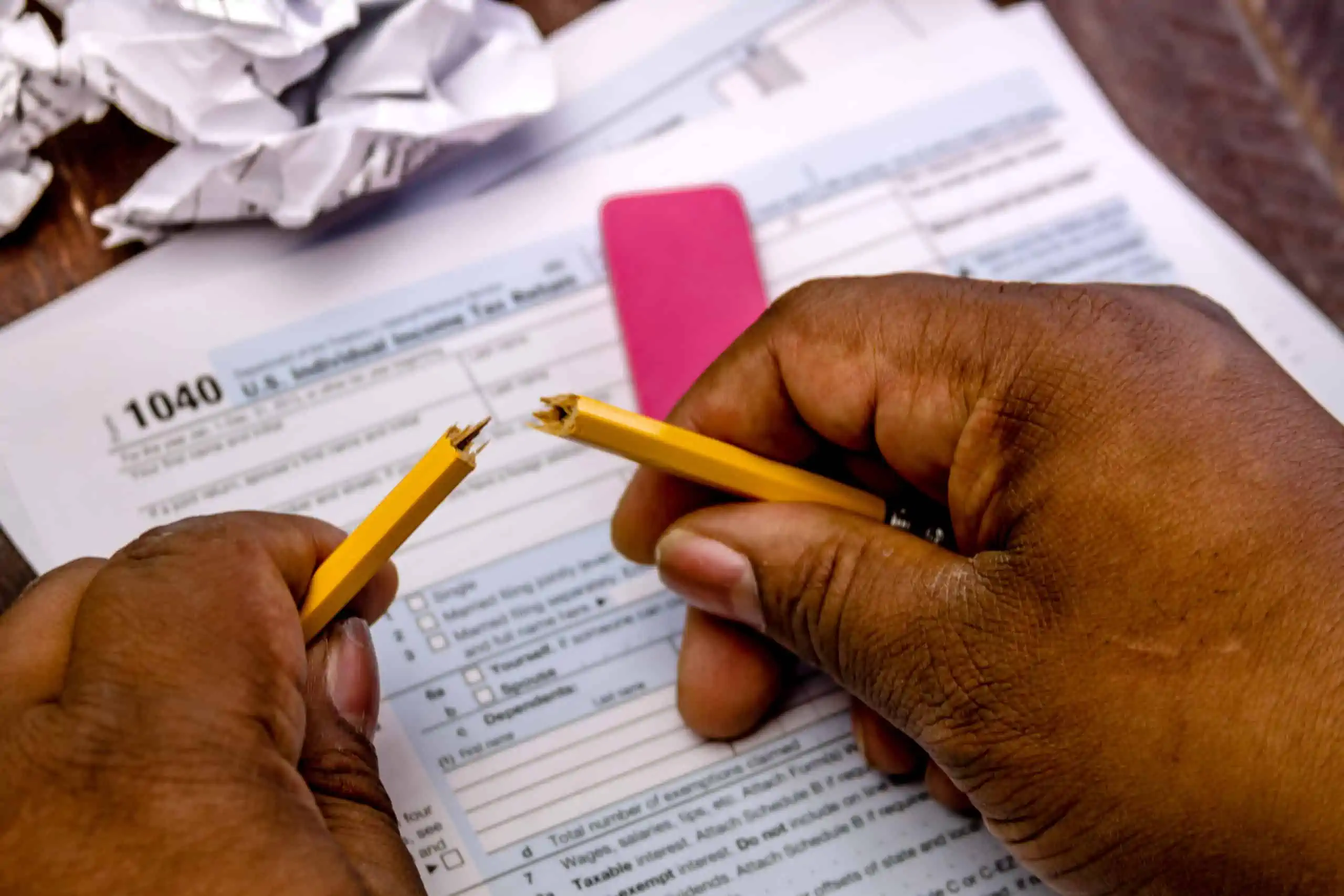 How to file taxes, a Black man holding a broken pencil with IRS Form 1040 Income Tax Return and crumpled up tax forms