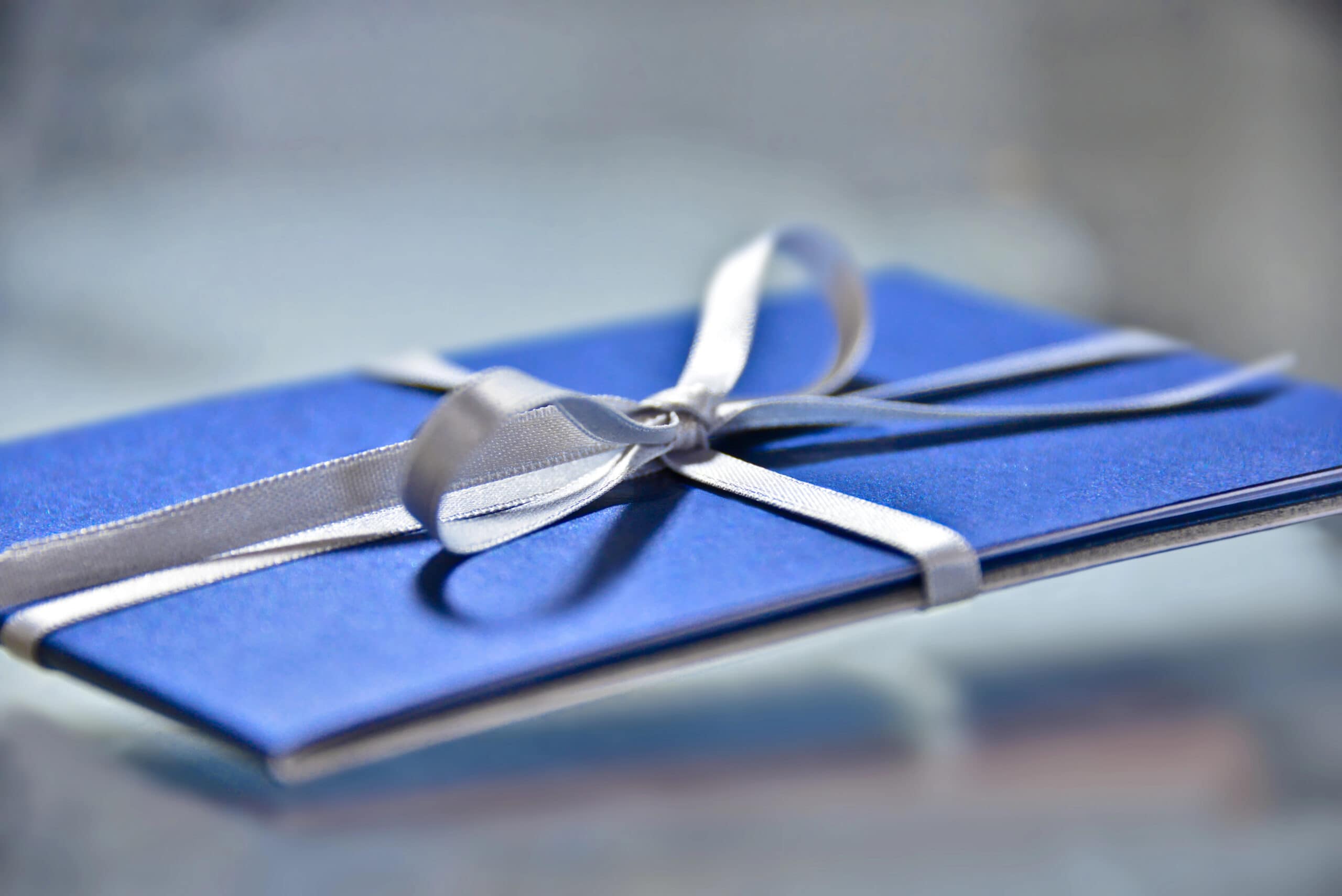 Are Gift Cards Are The Worst Product Ever? 1 Gift card wrapped in a blue folder with a silver stain ribbon tied in a bow.