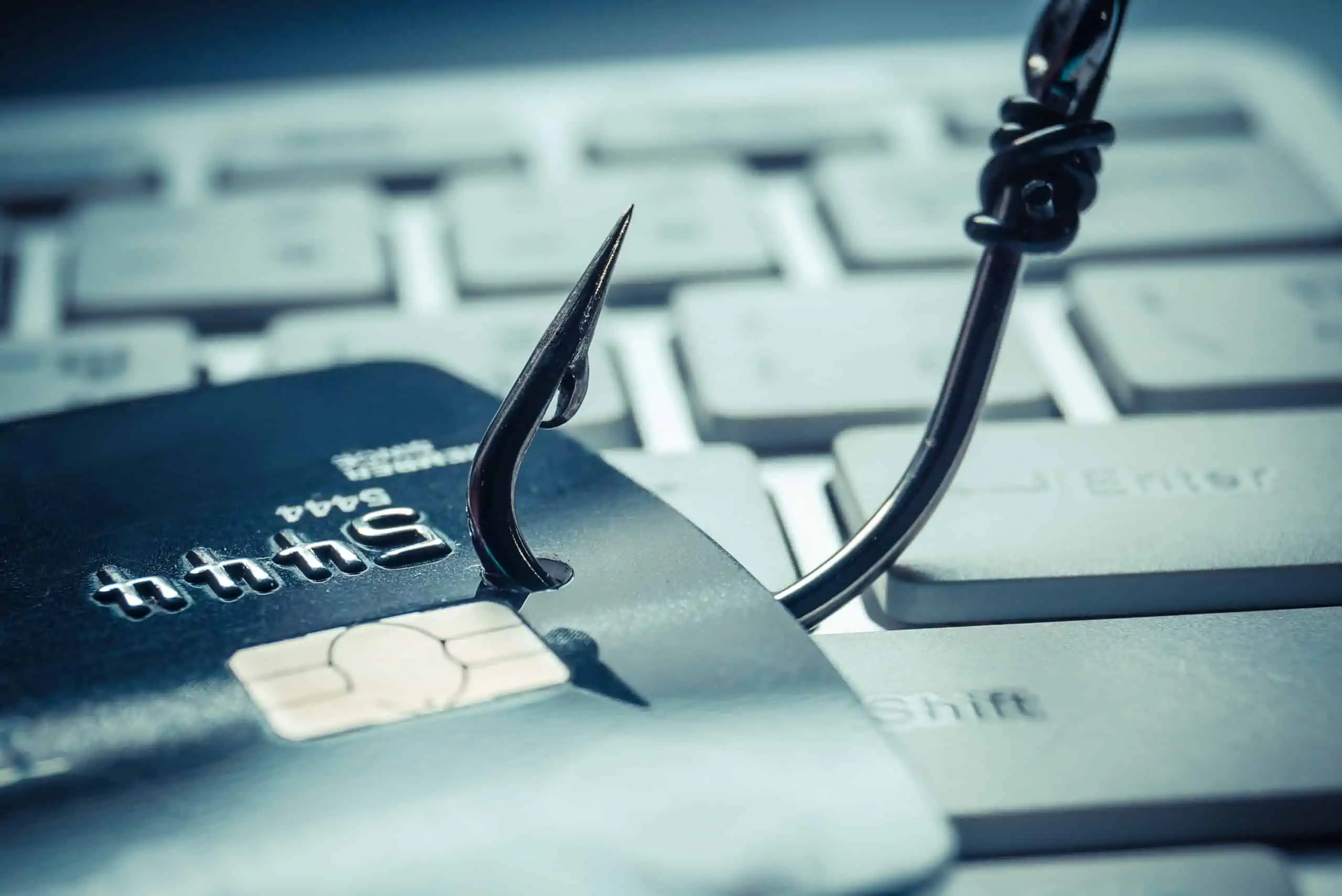 Phishing scam symbolized by a fishing hook put through a credit card sitting on a computer keyboard.