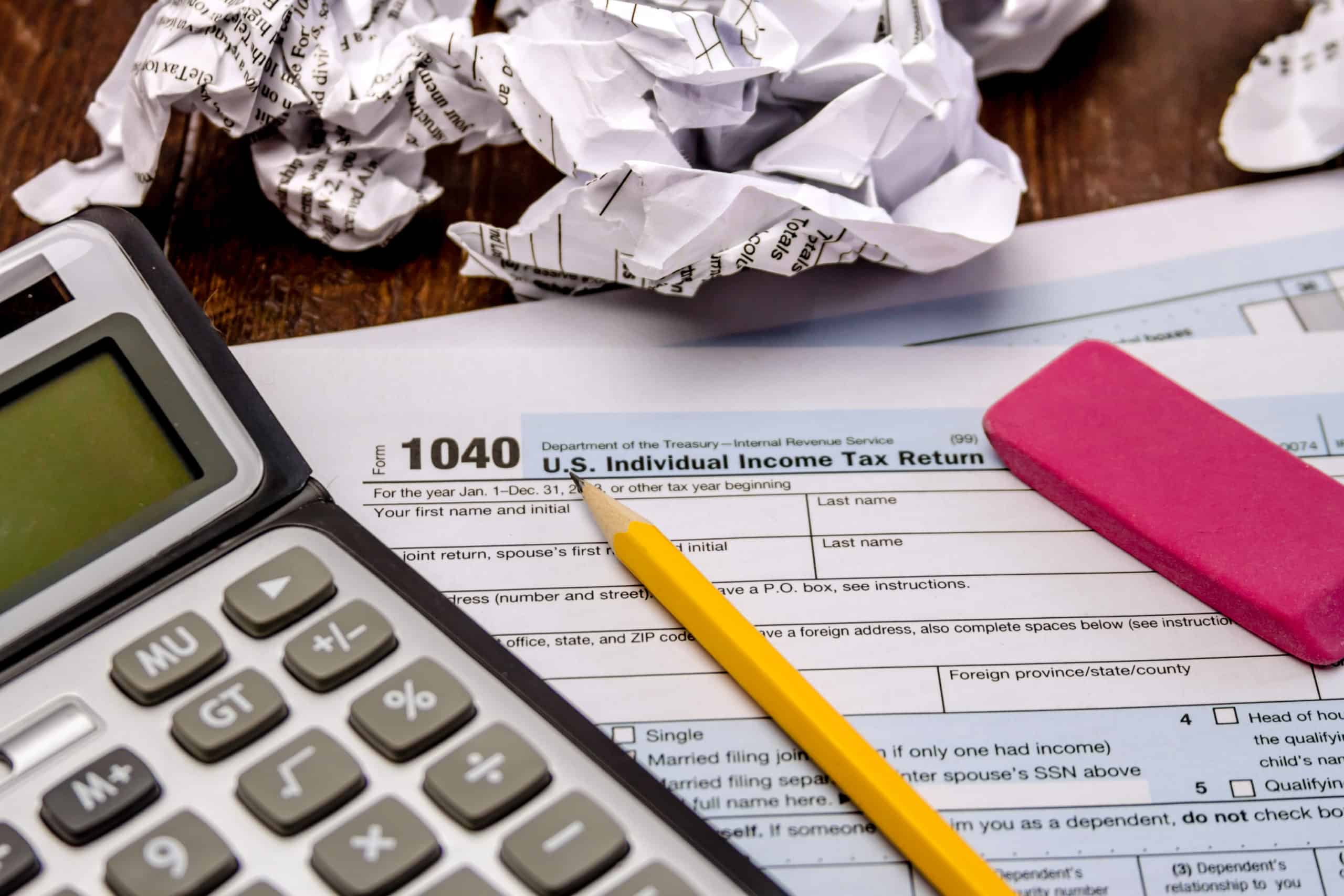 Income tax return Form 1040 with crumpled up forms, calculator, pink eraser and pencil