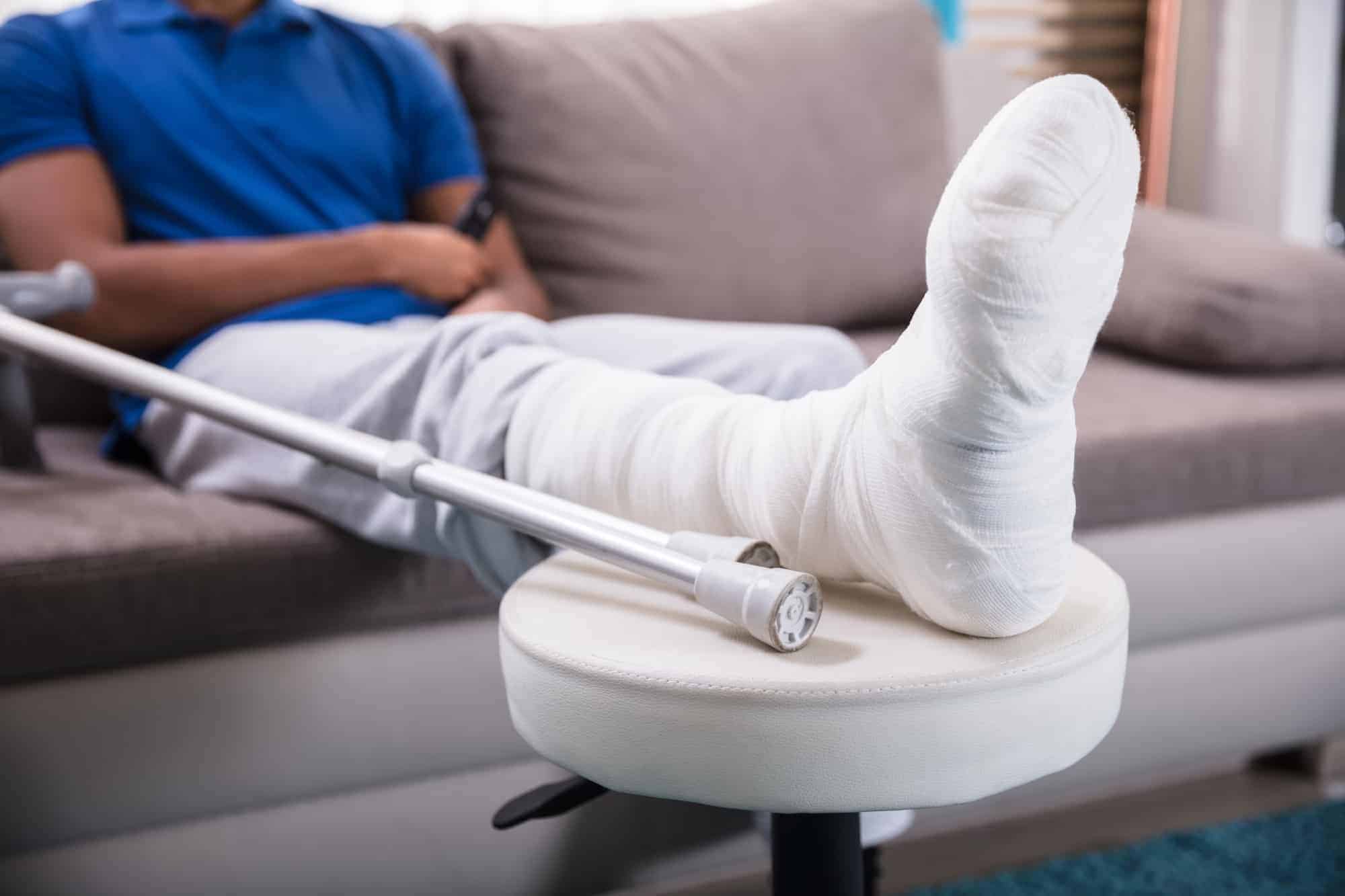 Do-It-Yourself Isn't Always Worth The Effort 1 Black man sitting on a couch with his foot wrapped and elevated after a do-it-yourself injury.