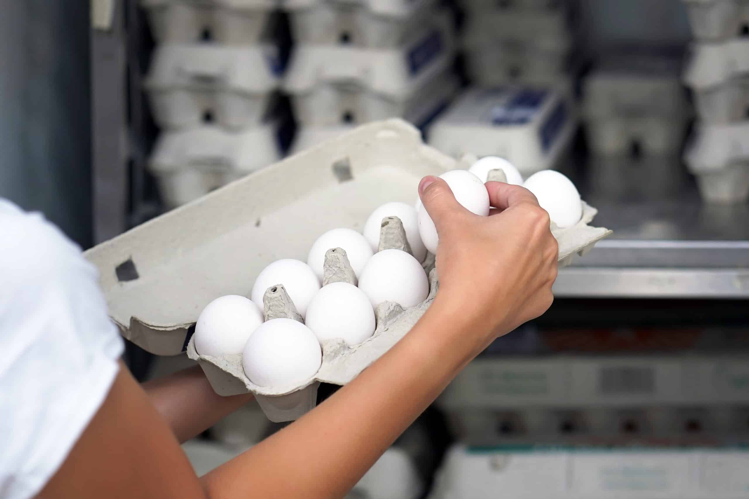 3 Reasons Instacart Grocery Delivery Service Is A Big No-Go For Me 1 Instacart shopper inspecting white eggs in a cardboard carton in front of egg cabinet at grocery store