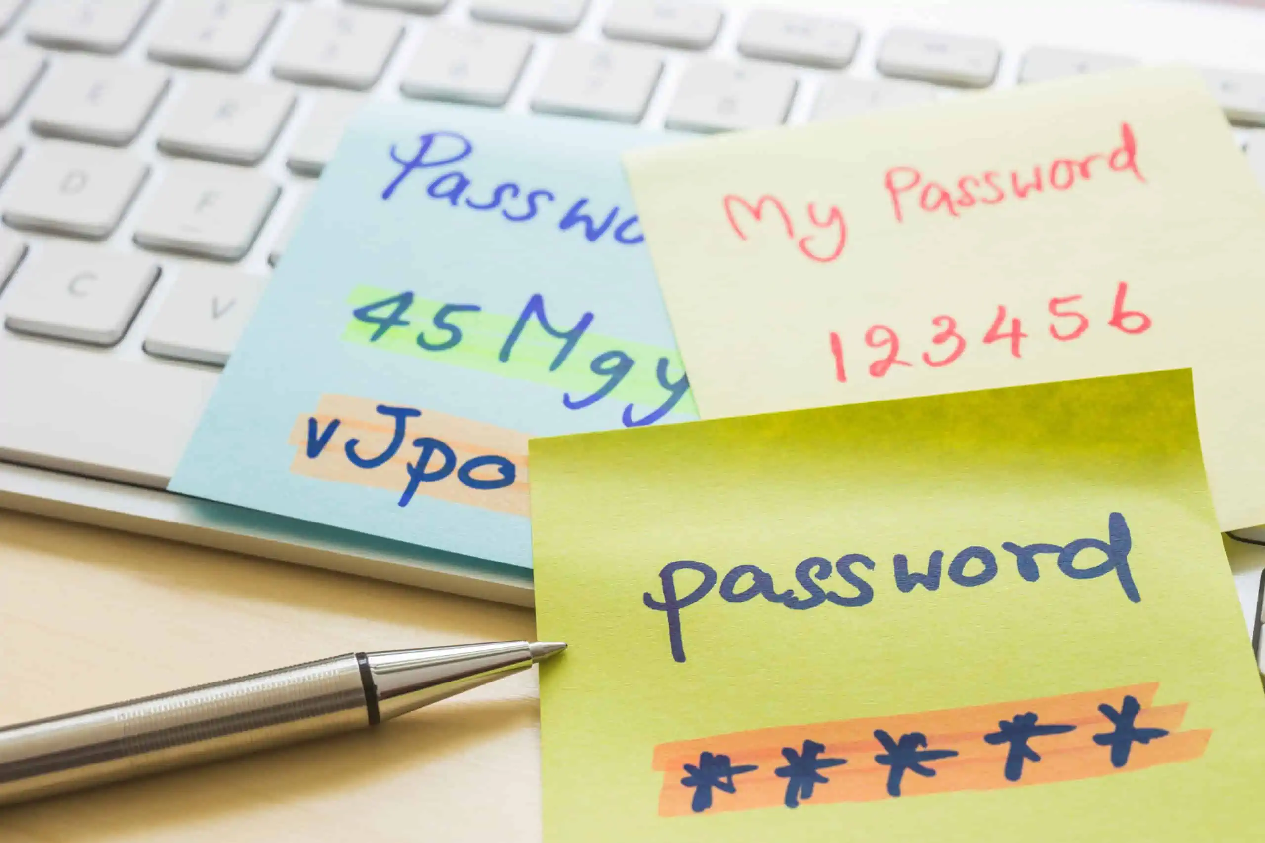 Silver pen and handwritten post-it notes for password sharing on top of a white Apple keyboard.