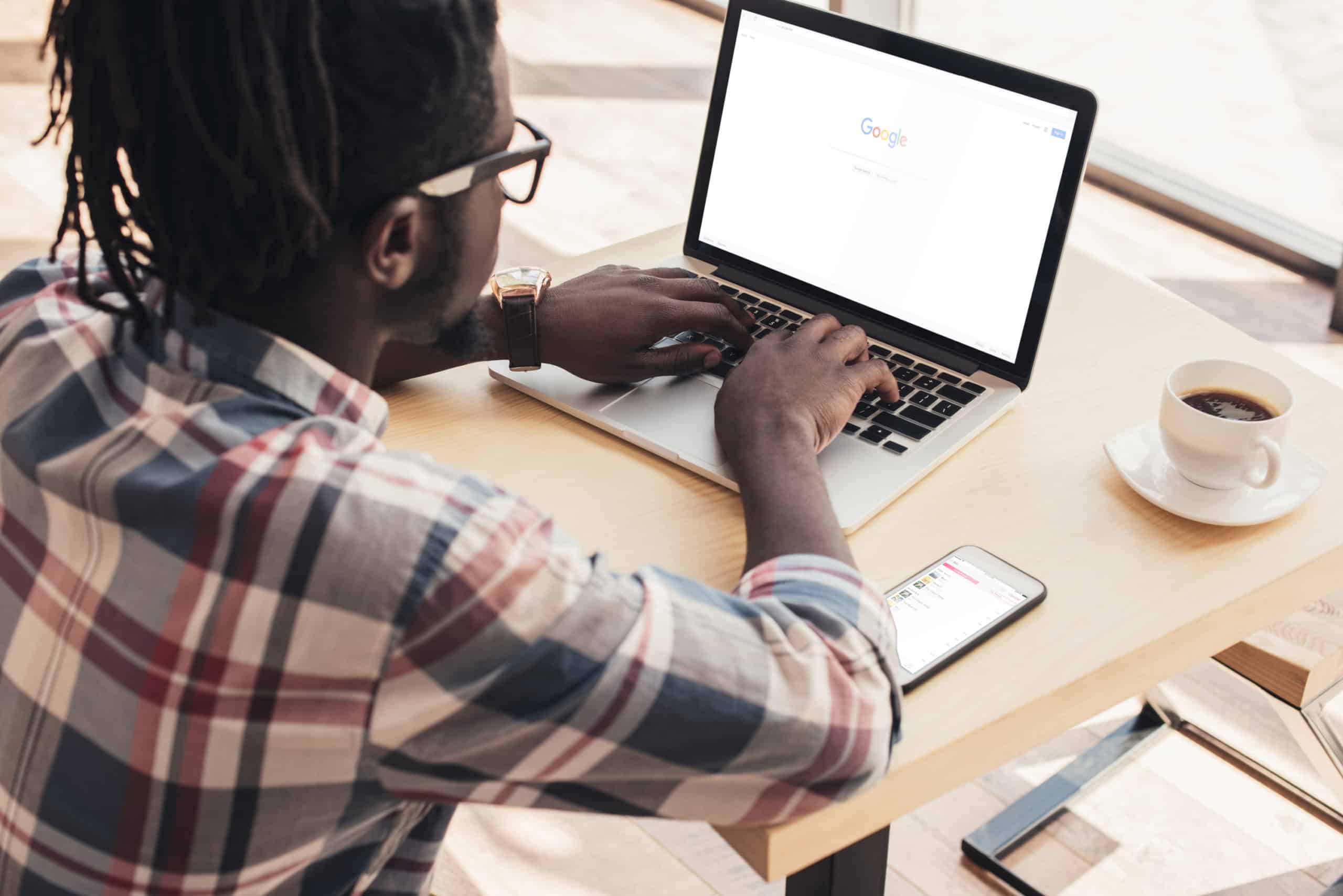 Black man with dreadlocks drinking coffee while looking state income tax info on a laptop