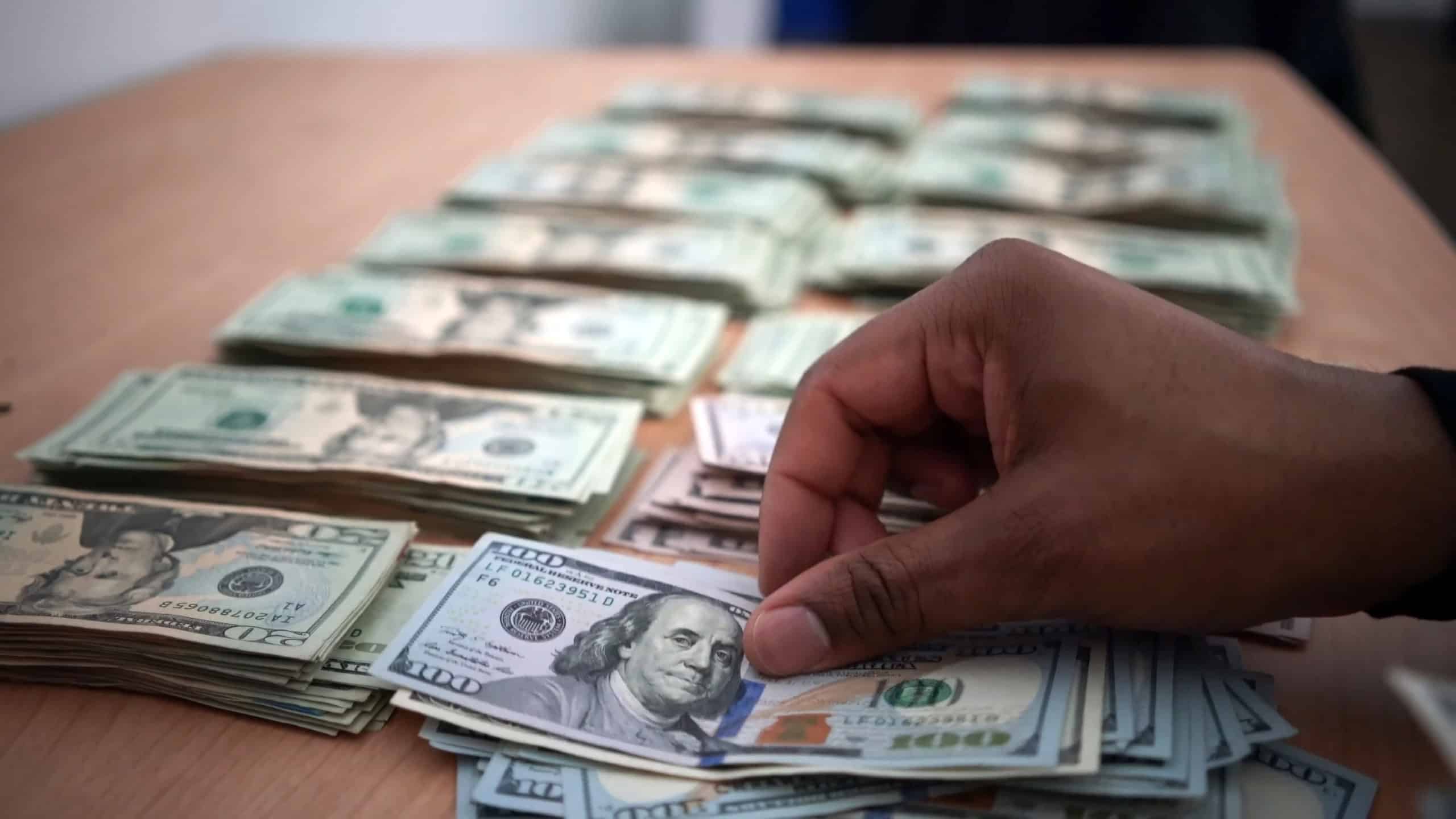 Closeup of a Black man's hand managing money by counting various denominations of dollar bills into piles on the wooden table