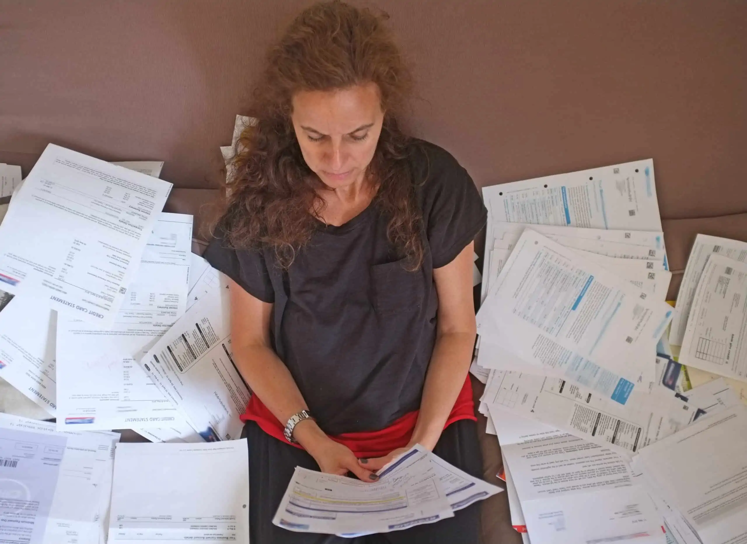 Caucasian woman sitting on a leather couch managing money by sorting through many financial documents
