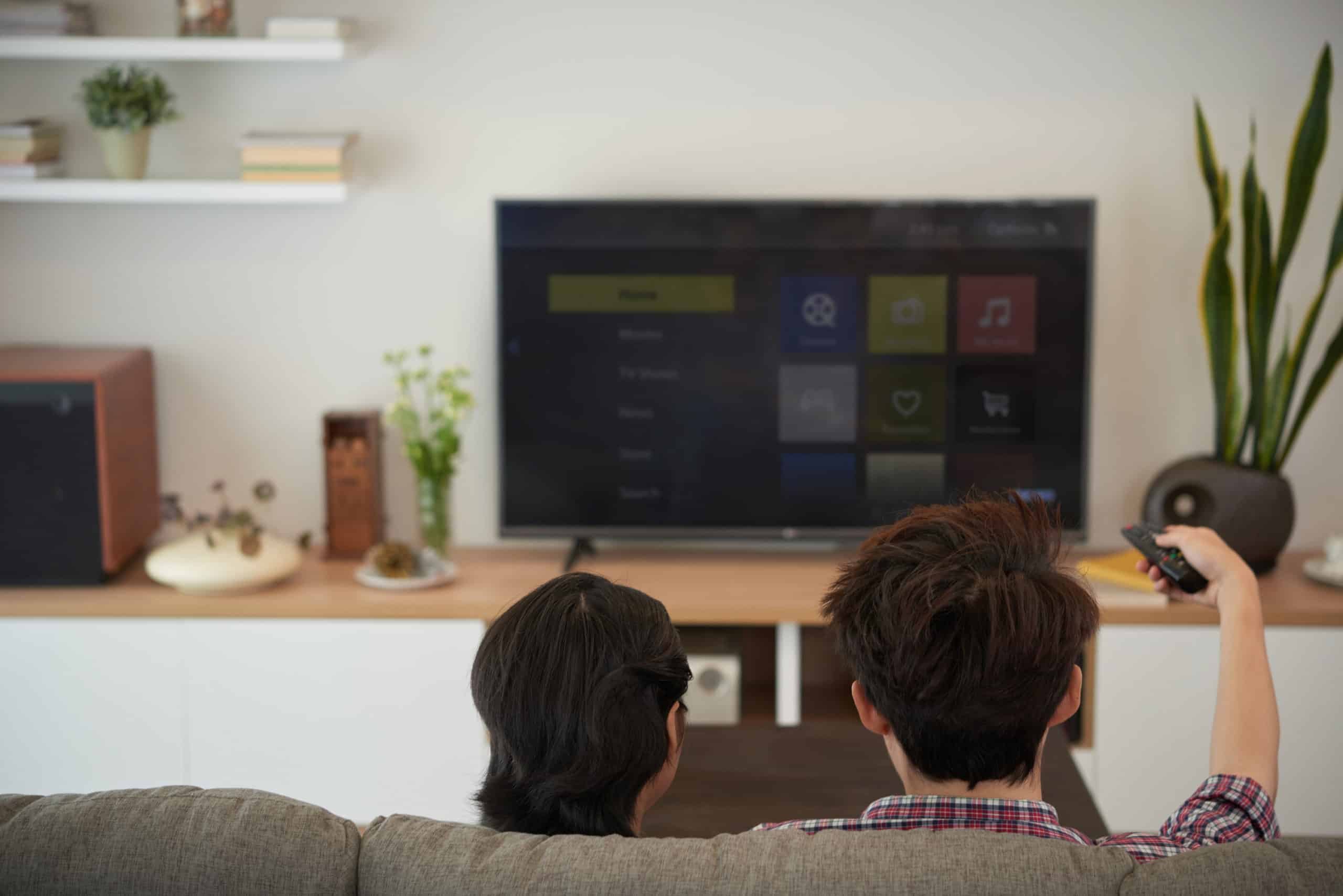 Couple on brown cloth couch watching televisions waiting for all of the marketing trick meant to make them spend money