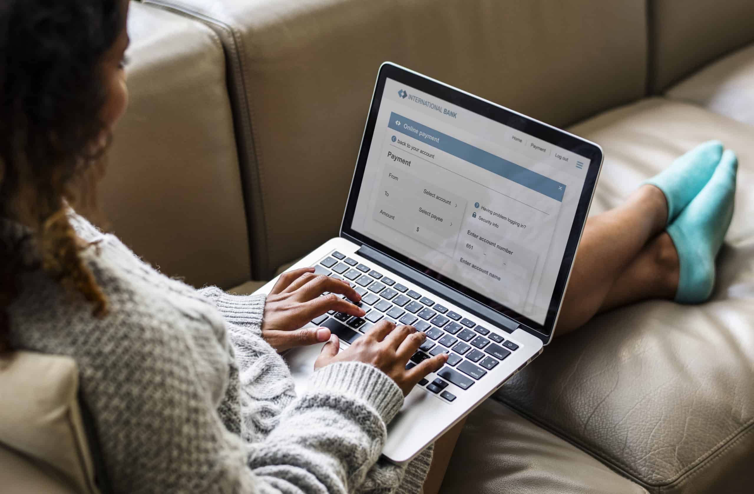 Black woman on a mauve leather couch making an online banking transfer.