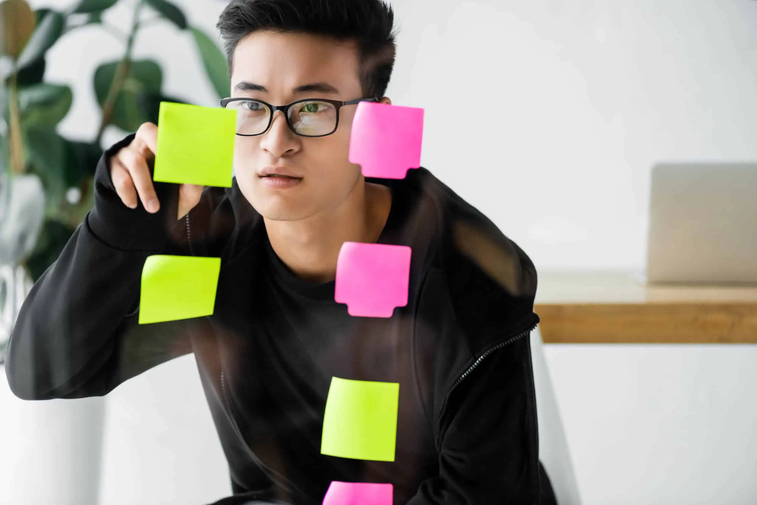 Young Asian man organizing Post-It notes containing a plan to implement financial advice on a glass board.