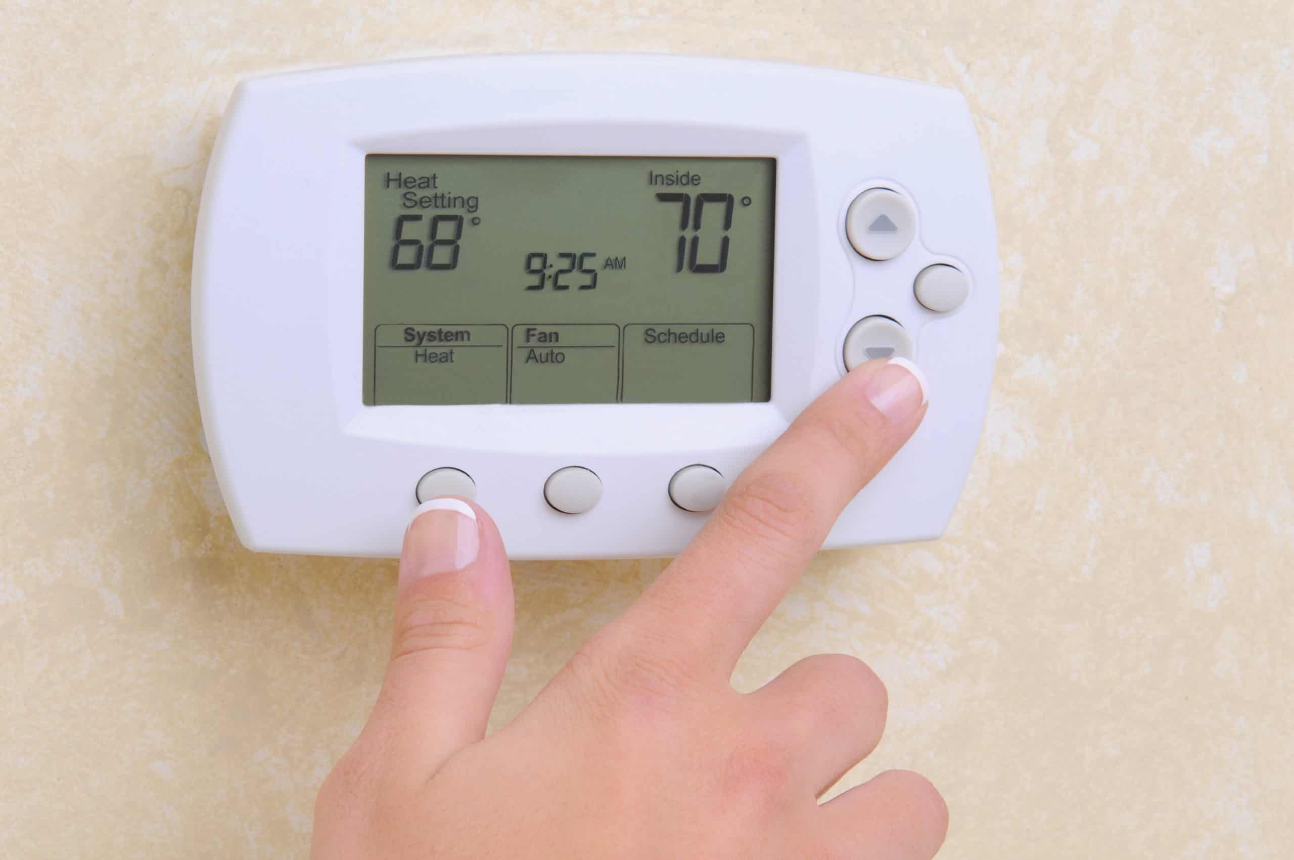 Honeywell programmable thermostat being controlled by an elderly man in a navy blue sweater.