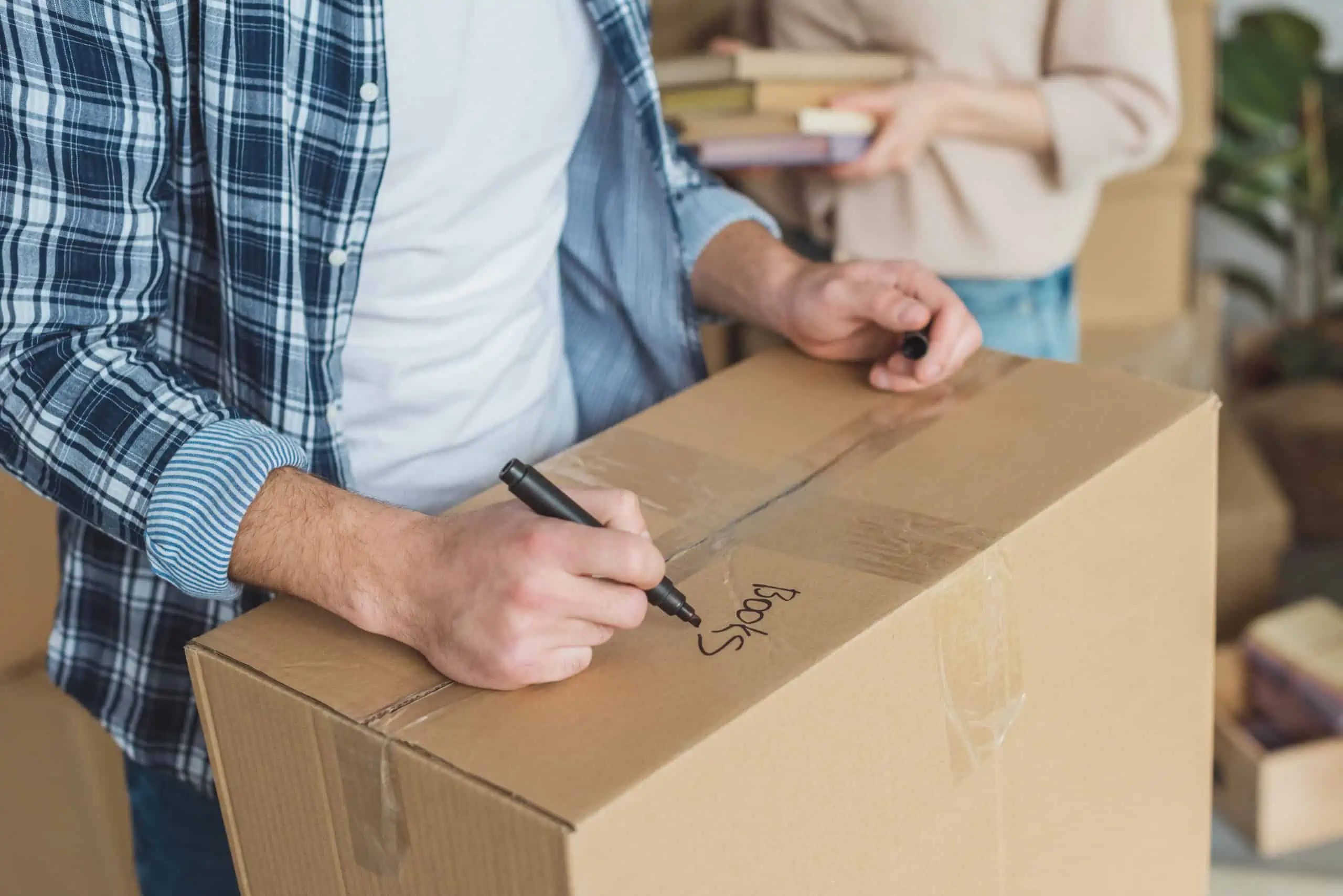 Man renting a home packing a moving box writing "books" in black marker
