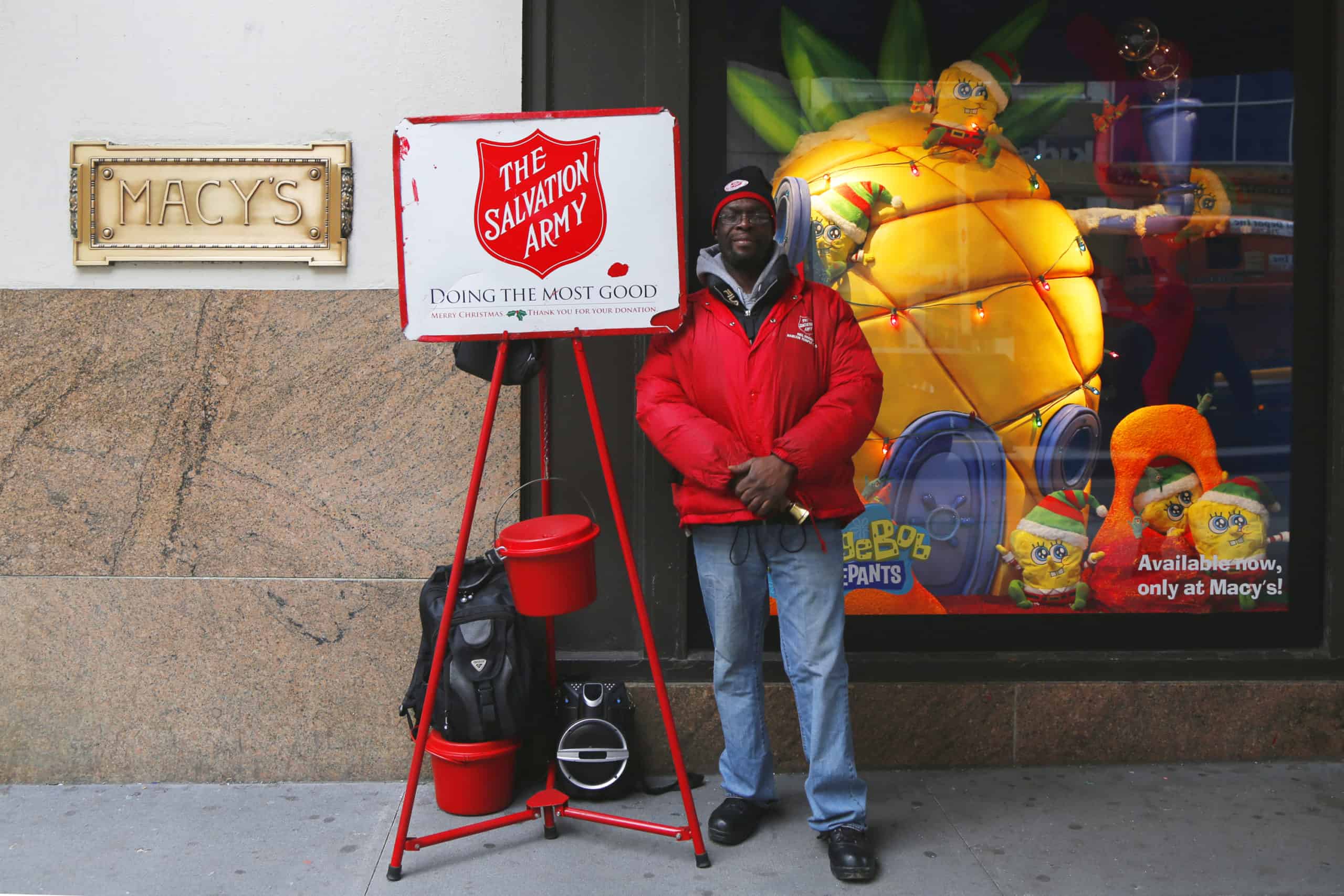 Black male Salvation Army volunteer standing next to the Red Kettle for people to make charitable donations for tax deductions.