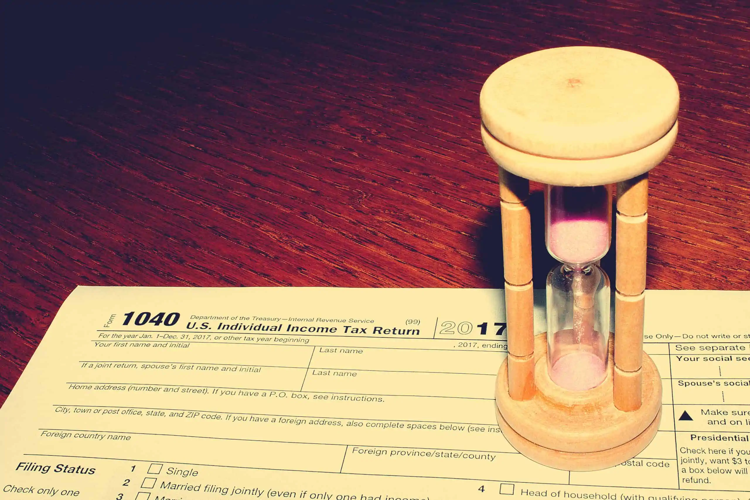 Income Tax Return, IRS Form 1040, on a red wood table with an hourglass running out, representing time for a tax extension