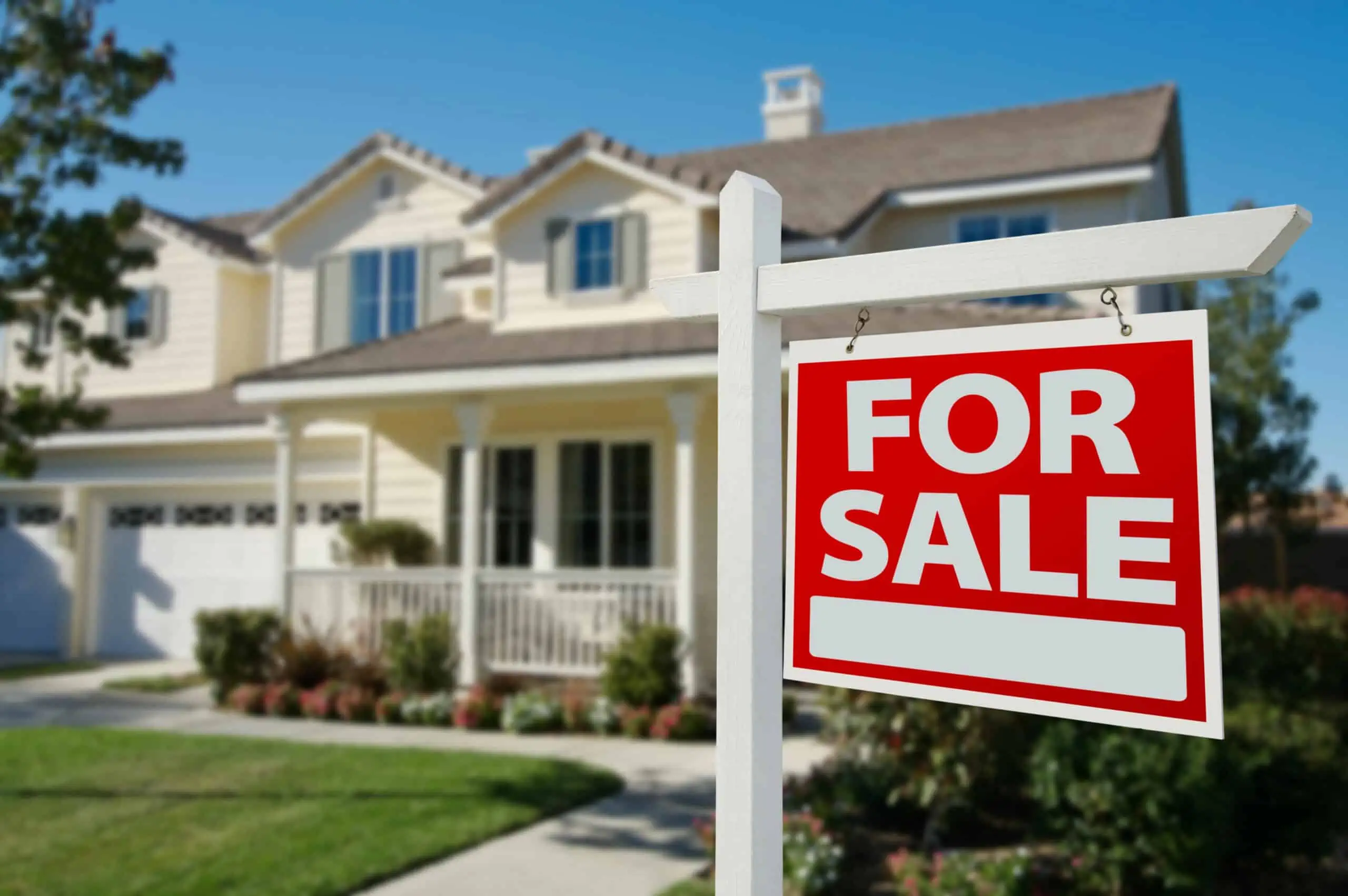 Red for sale sign hanging on a white wooden cross post in front of a attached single-family homes