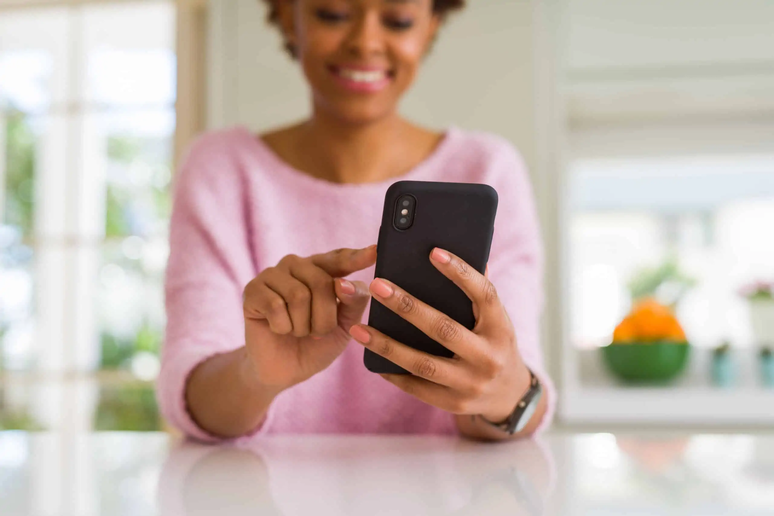 Black woman in a pink sweater using a smartphone and smiling