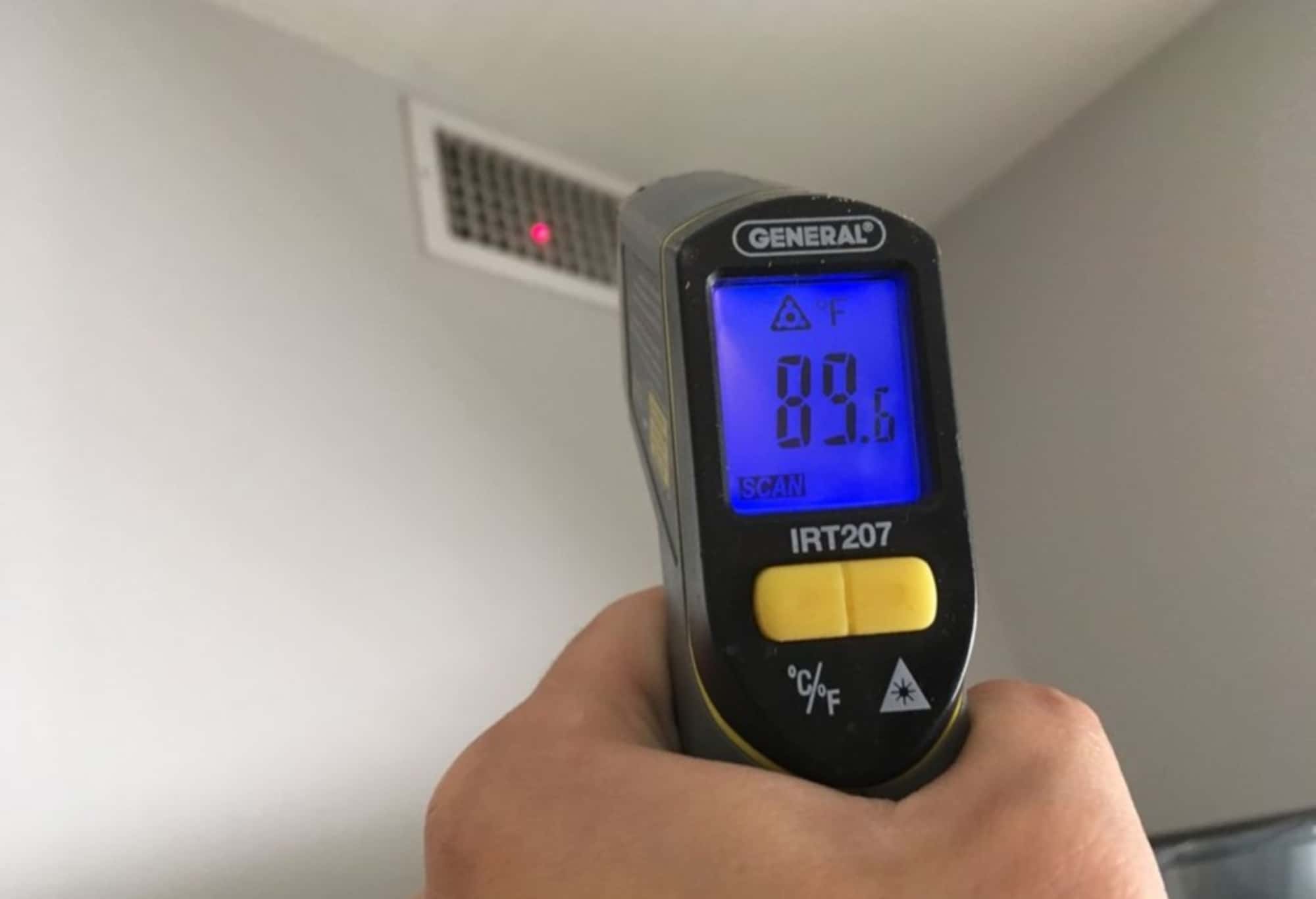 HVAC preventative maintenance performed by a certified HVAC technician using an infrared thermometer to test the temperature of air coming from a duct.