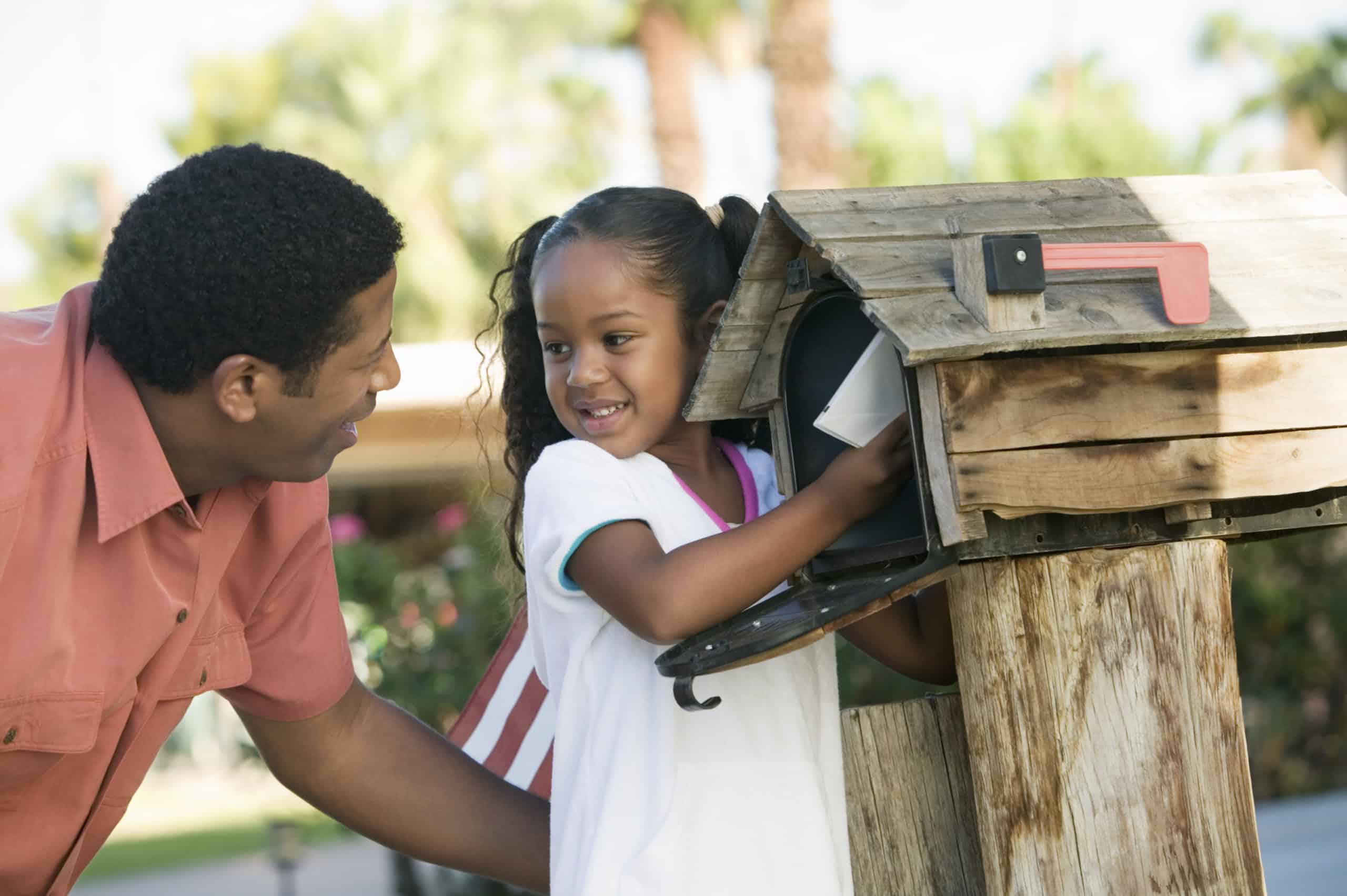 Black man and child checking a wooden mailbox for a state income tax refund.