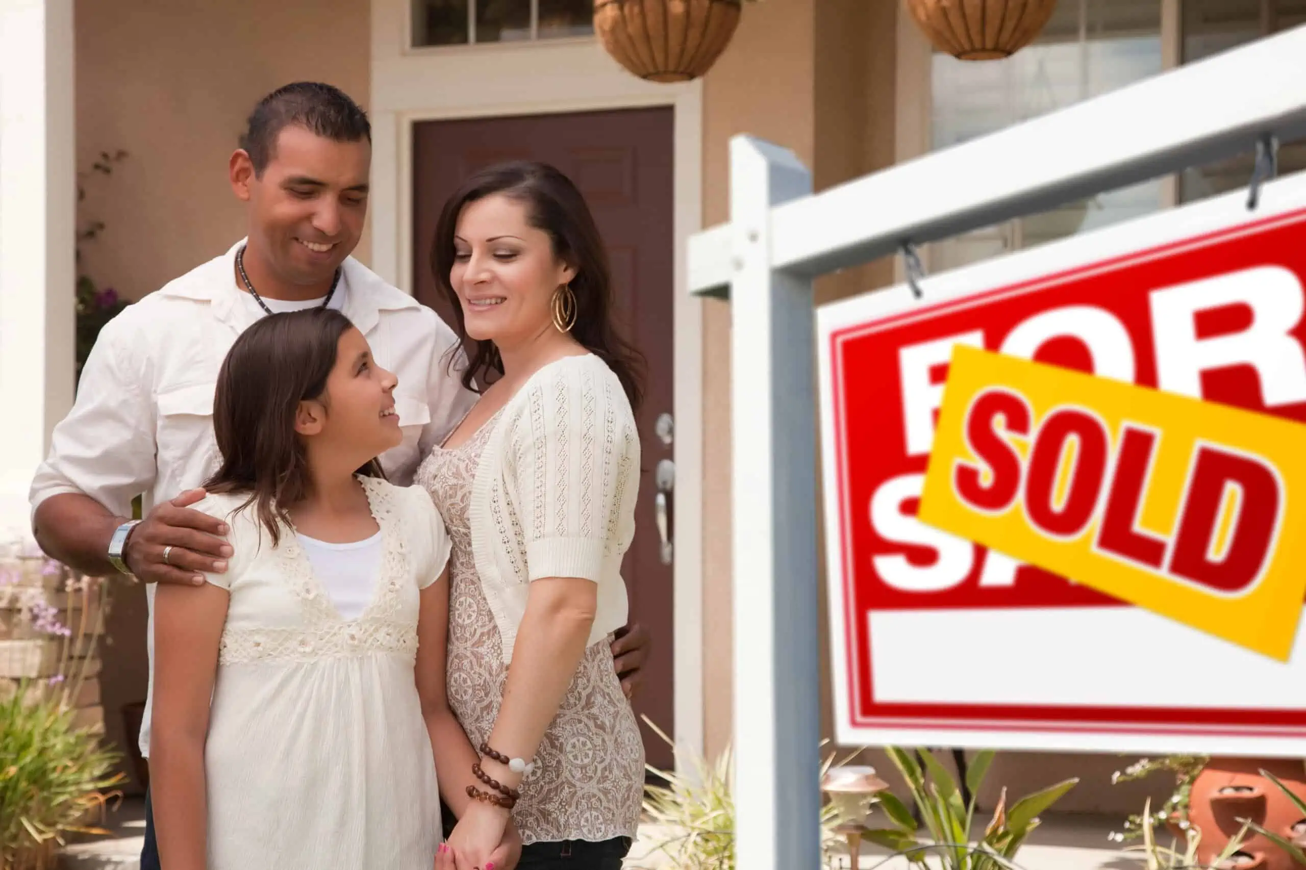 Hispanic Family in Front of New Home with a sold label covering the "For Sale" sign